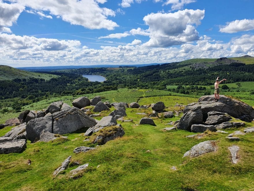 love is always open arms header shows the barefoot sub standing topless on a tor with a reservoir and dartmoor behind her, arms thrown up and back to embrace the world.