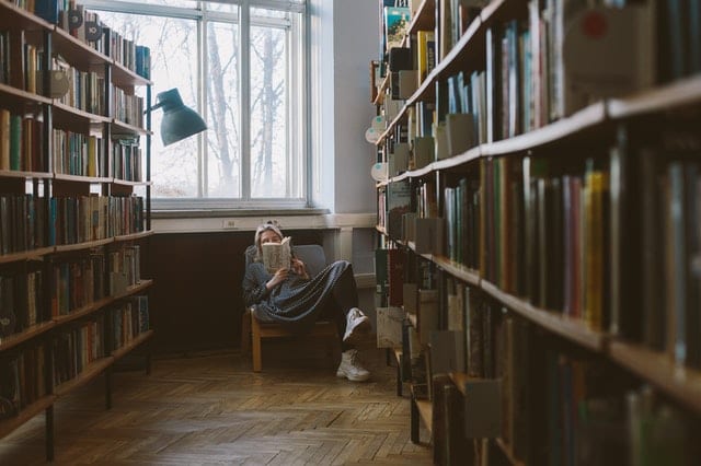 lady sitting in a chair between bookshelves for post My Library of thought