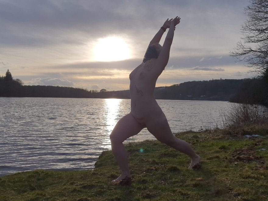 Naked lady doing outdoor yoga: Lakeside warrior pose