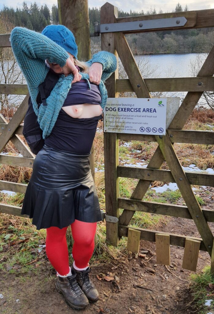 Puppy play or scavenging, the barefoot sub exposes her breasts at a sign for the dog exercise area
