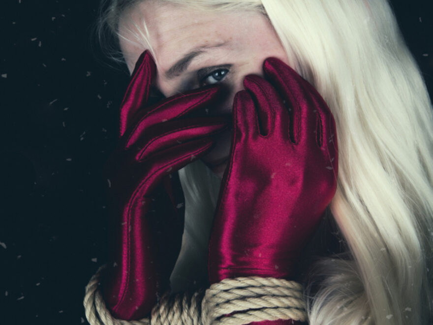 Creating the best day header image shows a woman with long blonde hair peeking through hands which are wearing long, red satin gloves and are bound at the wrist.