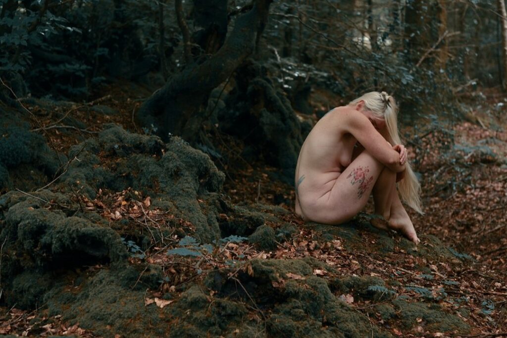 a life without regrets header shows blonde lady sitting on the woodland floor, curled over her legs with head buried into her knees, and blonde hair falling over arms and legs.