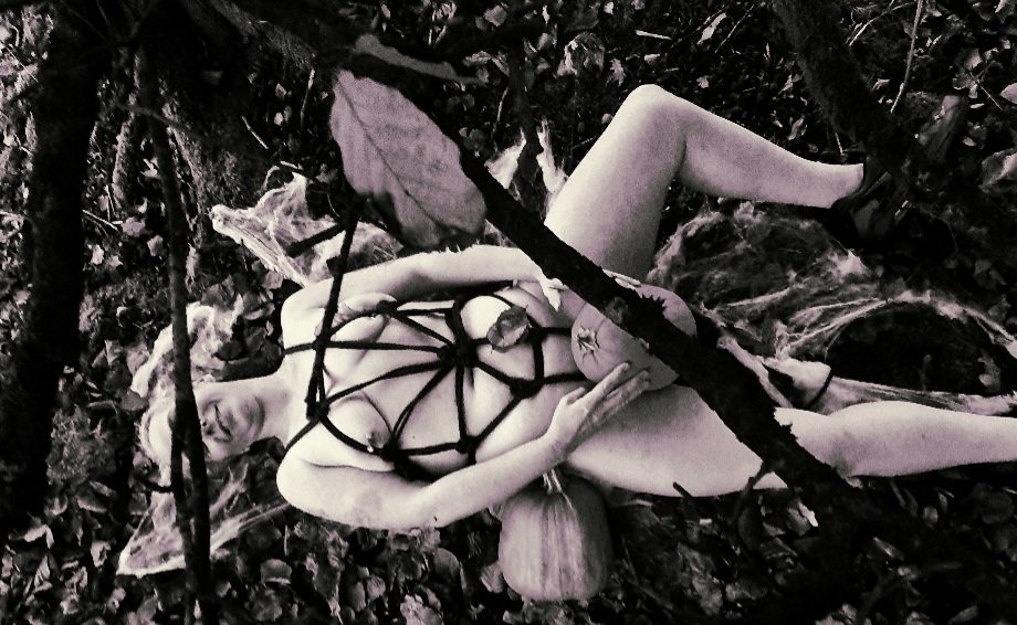 Autumn is my favourite season header image shows black and white image of a lady lying on the forest floor, tied in a spider web design and holding a pumpkin.