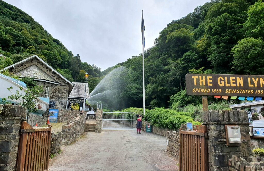 Flagpoles and fountains header image shows a lady exposing her breasts under a flagpole at the Glen Lyn Gorge entrance. There is a large spray of water behind her, and the gorge is surrounded by trees.
