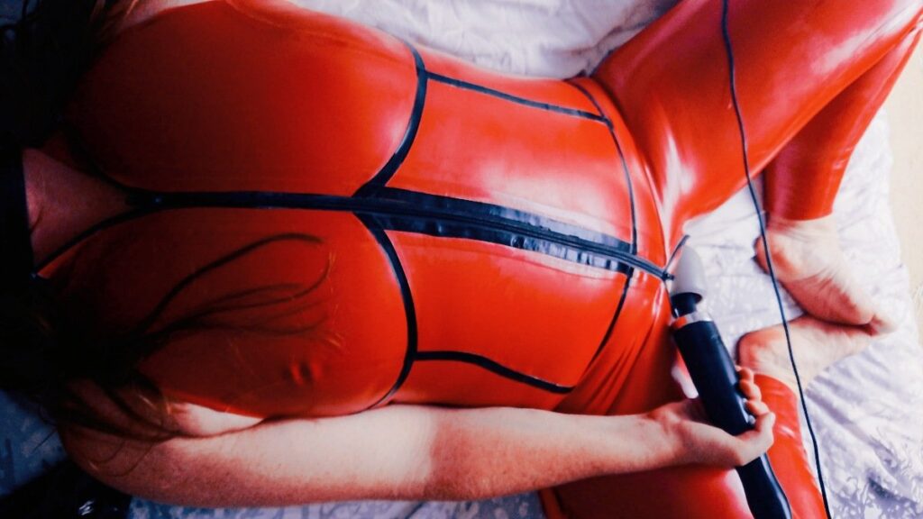 relaxing in rubber red catsuit with black trim with a doxy pressed to the open crotch.