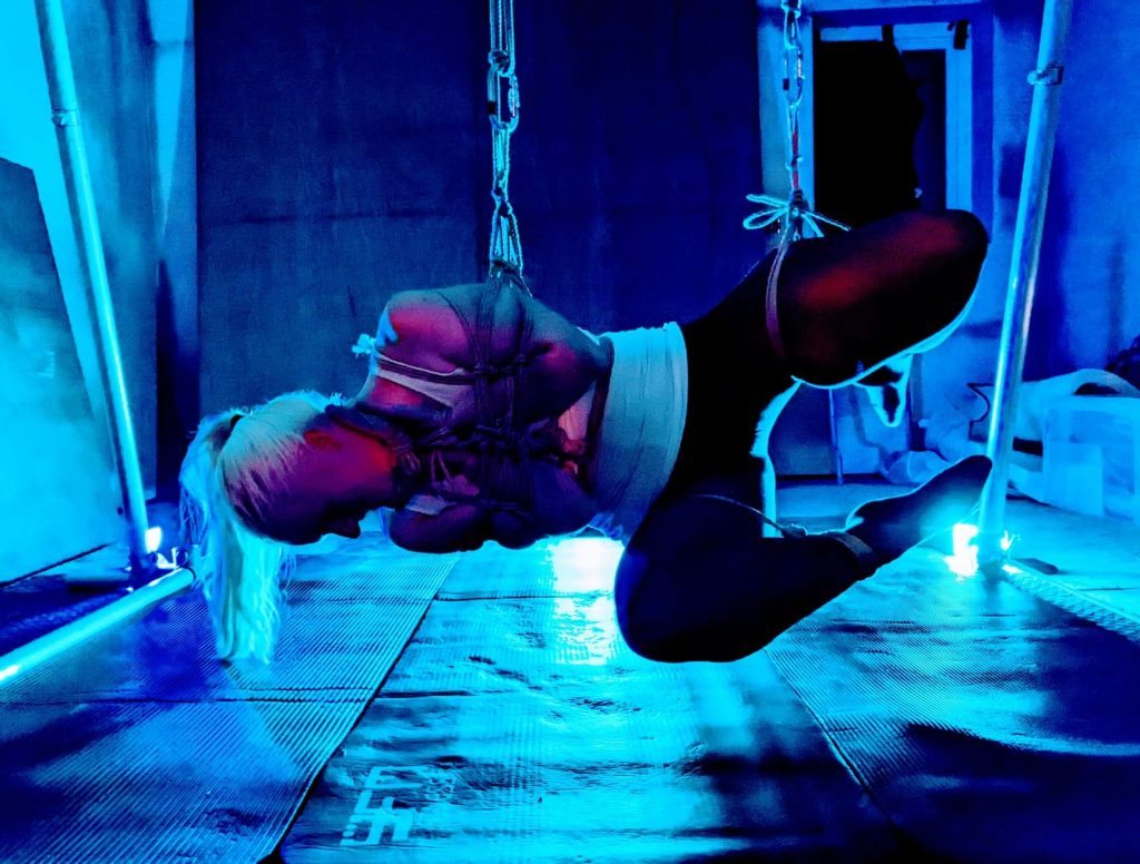 Lady in tights and a vest Backlit and bound in a sideways suspension