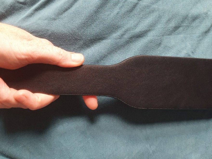 Bondage couture paddle being held in the left hand.