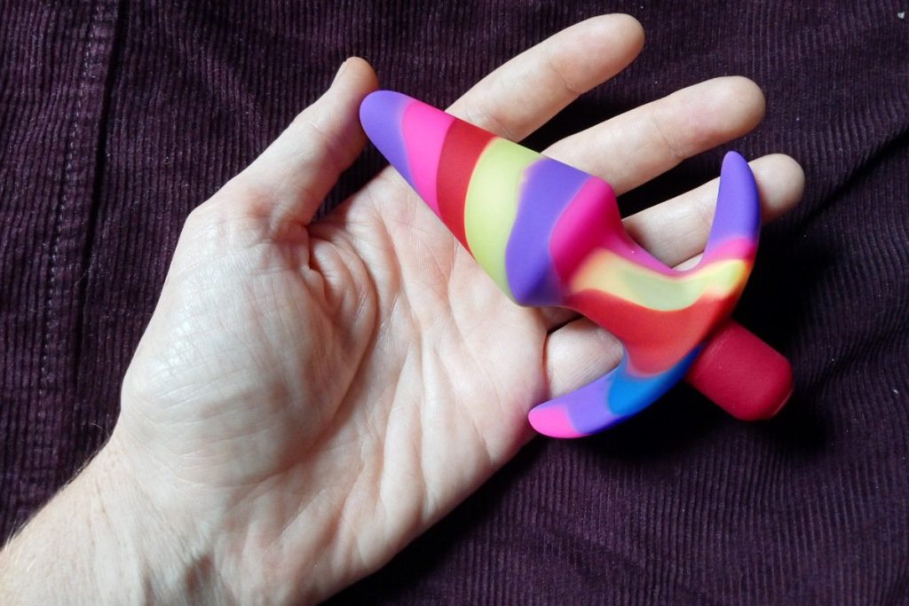 anal august for the free spirit header shows a rainbow coloured butt plug resting on my open hand.