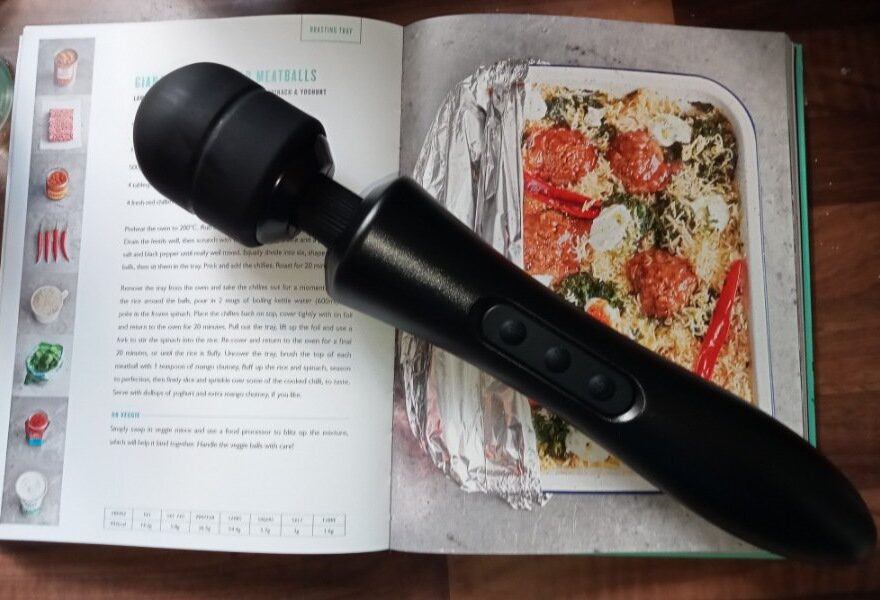 The black, super powerful massager laying on top of an open cookery book showing a recipe for giant meatballs.