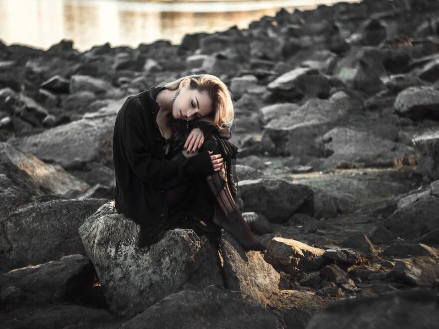 "No song in your heart? Sing anyway" header shows woman sitting on a rocky beach, wearing a black dress, hugging her knees.