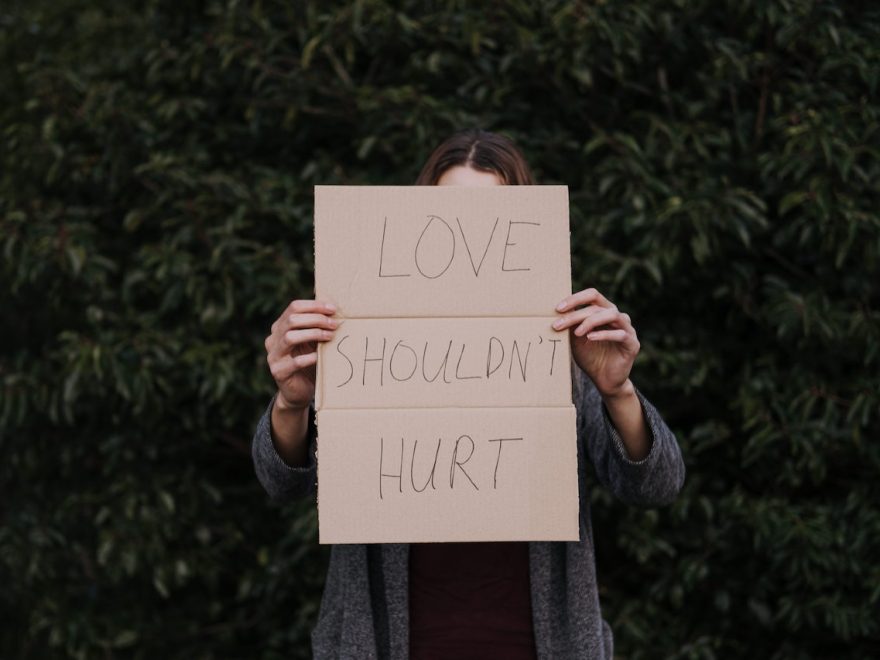 Embracing vulnerability header shows a woman holding up a sign saying "LOVE SHOULDN'T HURT"
