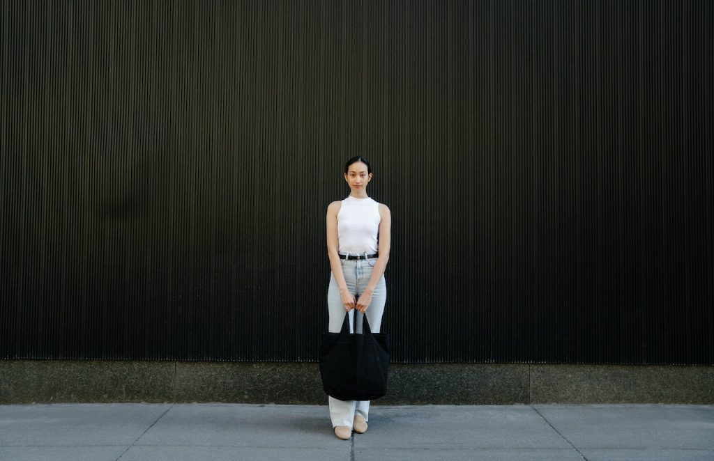 Self esteem rises header shows woman standing with a black bag in her hands, in front of a black wall. 