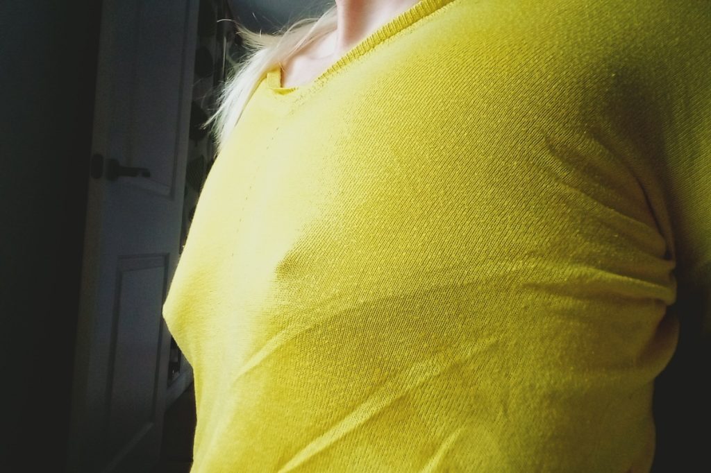 finely knitted yellow sweater being worn over bare breasts and erect nipples.