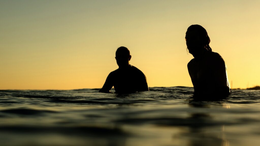 Two people silhouetted in the sea at sunset is the header image for A Letter To My Hero