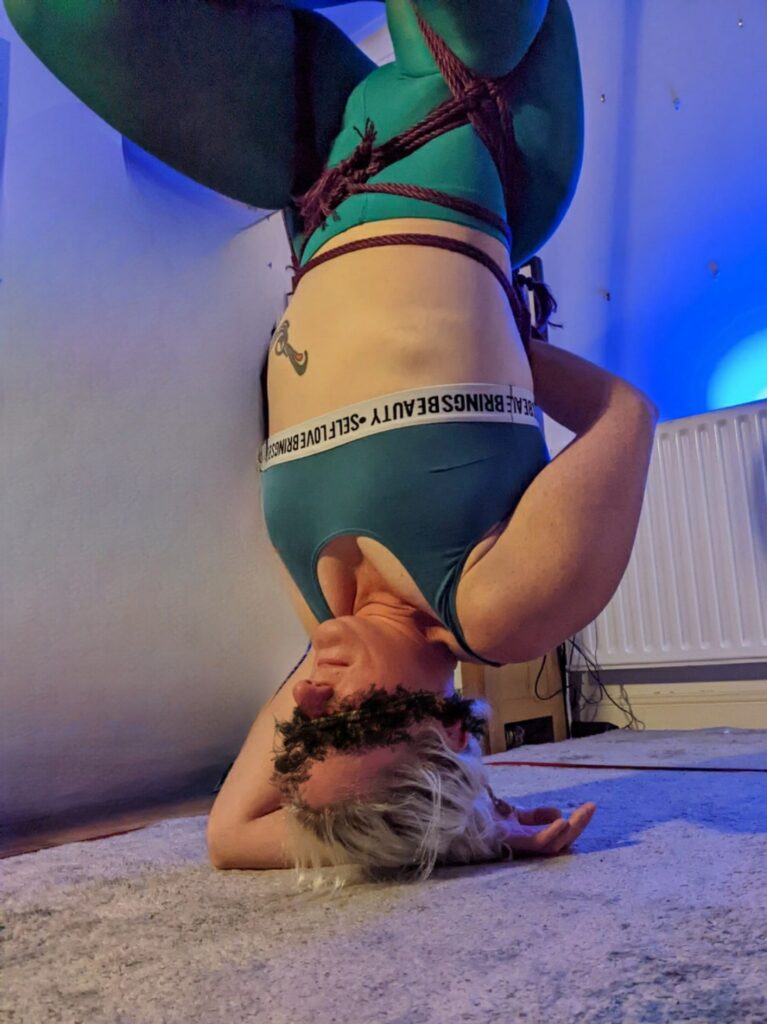 Fear Of header image shows me in an inverted rope suspension. Turquoise bra and tights, and hip harness in purple rope. 